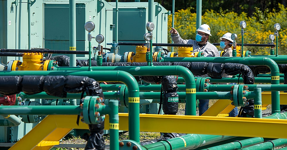 two workers in masks looking at rig site network of equipment