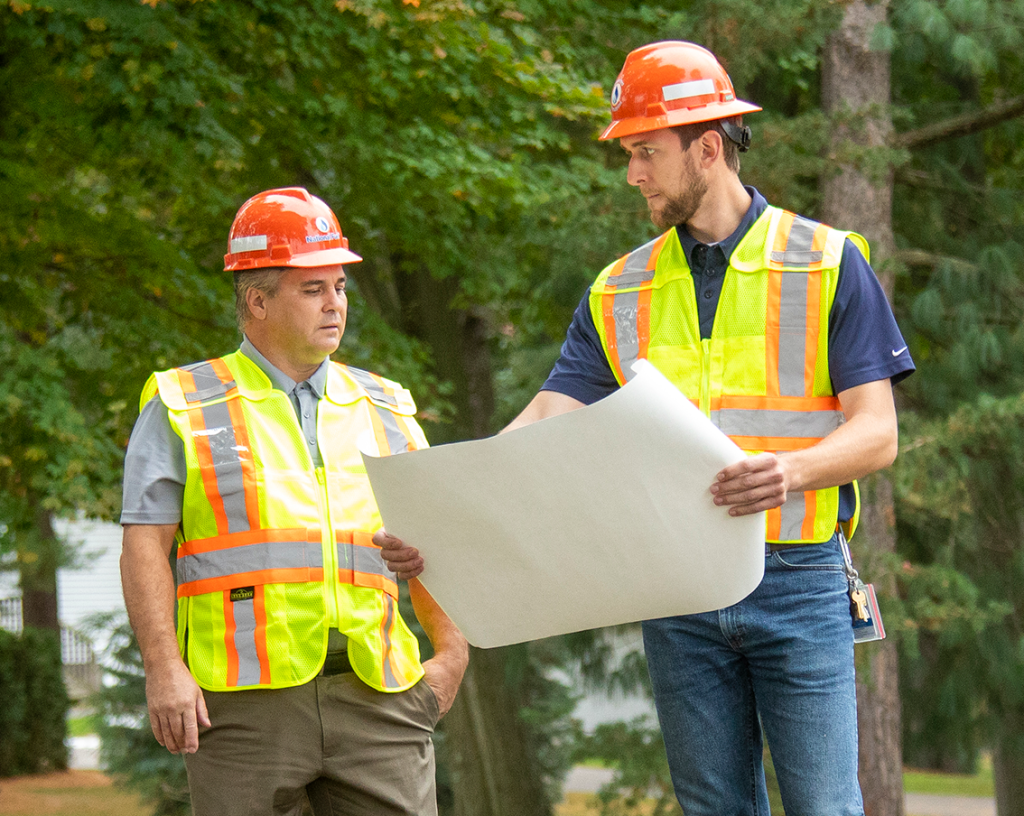 two men looking at a paper talking in front of pipe marker