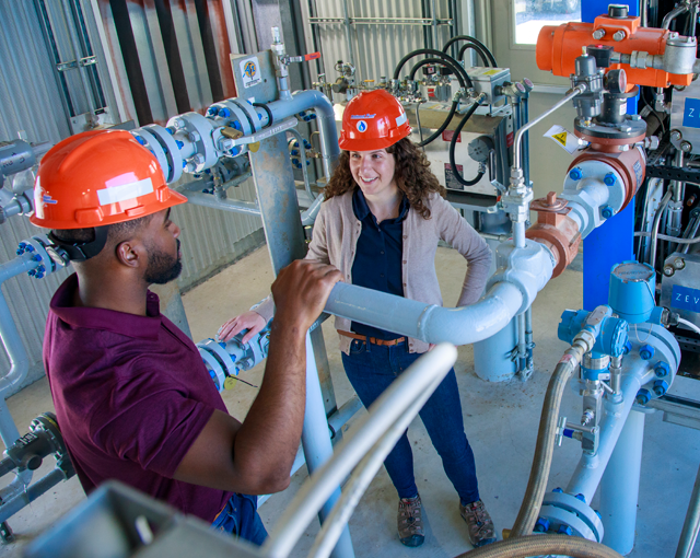 man and woman talking in hard hats next to ZVAC machine