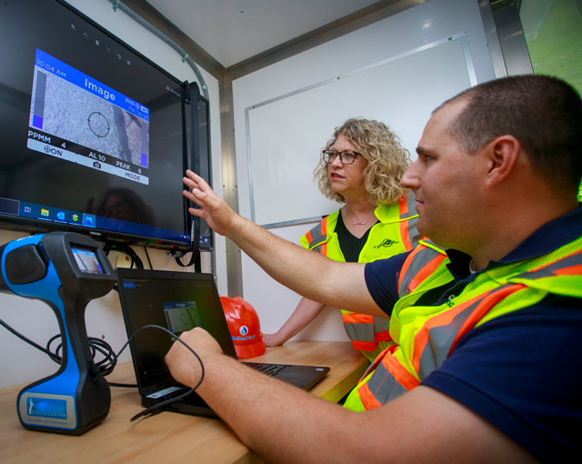 man pointing to computer showing woman an image on a tv