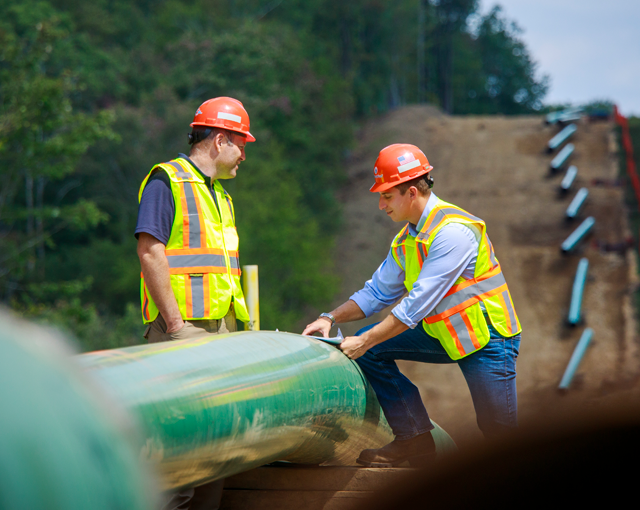 two men talking at a worksite wearing hard hats and vests