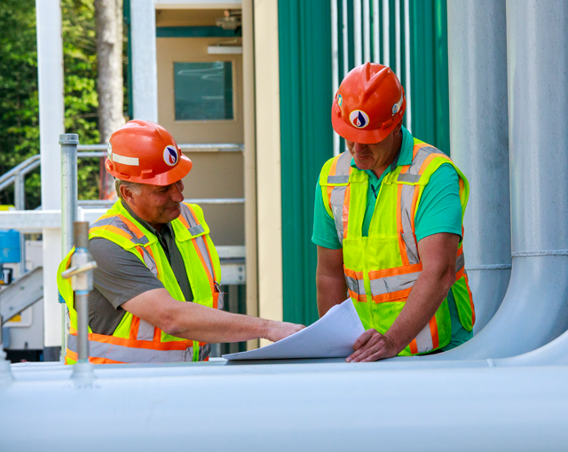 two men reading paper talking and pointing while wearing hard hats