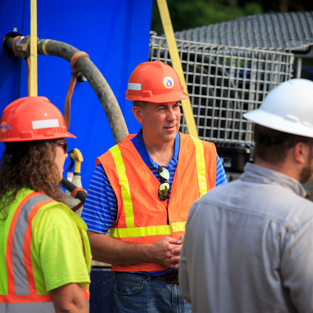 group of people in a circle talking with hard hats and vests