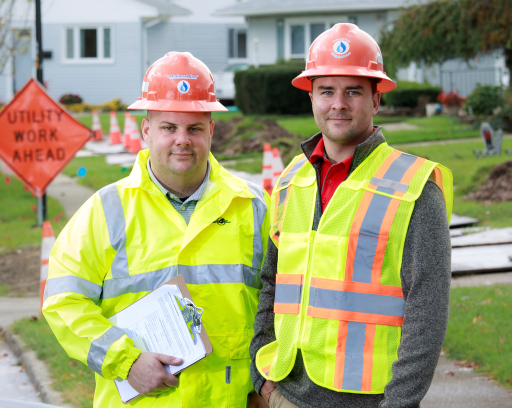 two utility workers in front of worksite wearing hard hats and vests